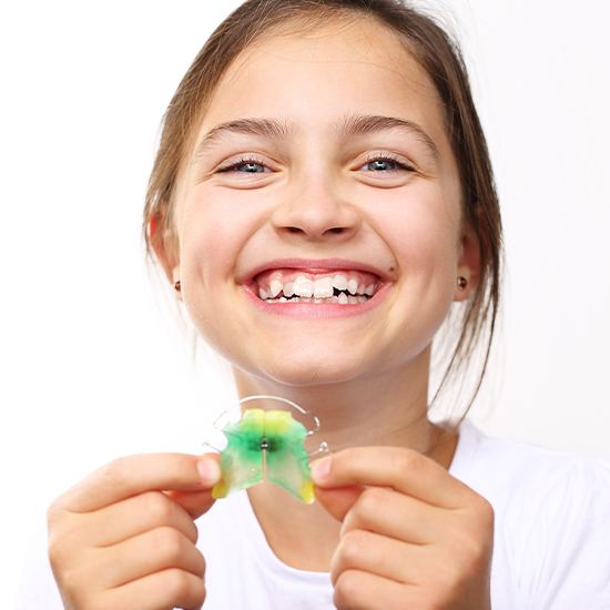 Young girl with holding up an orthodontic appliance smiling