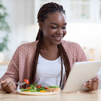 Woman with braces smiling and looking at tablet while eating