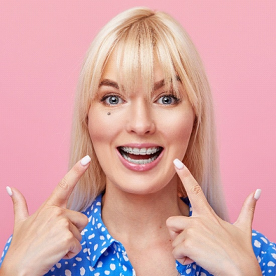 A young female pointing to her braces after seeing an orthodontist in Worcester